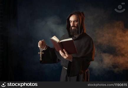 Medieval monk praying with book in hands in church, secret ritual. Mystery and spirituality. Medieval monk praying with book in church