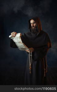 Medieval monk reads a prayer in the ancient manuscript, religion. Mysterious friar in dark cape. Mystery and spirituality