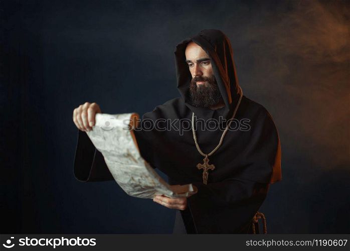 Medieval monk with an evil face reads a prayer in the ancient manuscript, religion. Mysterious friar in dark cape. Mystery and spirituality. Medieval monk with an evil face reads a prayer