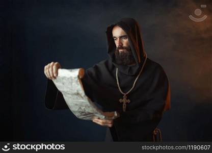 Medieval monk with an evil face reads a prayer in the ancient manuscript, religion. Mysterious friar in dark cape. Mystery and spirituality. Medieval monk with an evil face reads a prayer