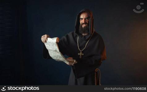 Medieval monk with an evil face reads a prayer in the ancient manuscript, religion. Mysterious friar in dark cape. Mystery and spirituality