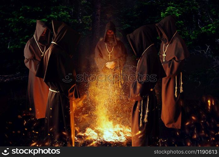Medieval monks praying against a big fire in the night, secret ritual. Mysterious friar in dark cape. Mystery and spirituality