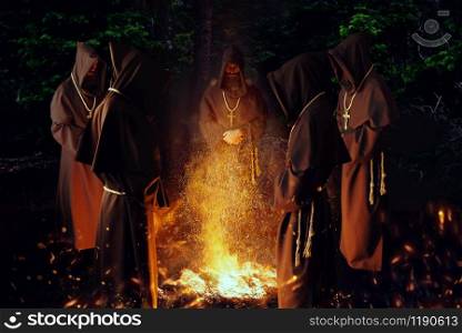 Medieval monks praying against a big fire in the night, secret ritual. Mysterious friar in dark cape. Mystery and spirituality