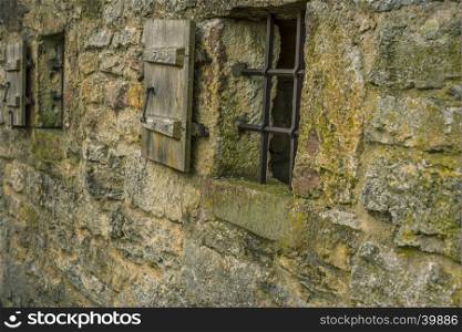 Medieval stone wall with two small windows, fortified with metal bars