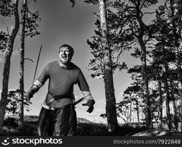 Medieval viking warrior wearing chainmail and he has the sword, north nature on background, black and white image