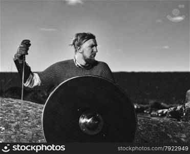 Medieval viking warrior wearing chainmail, he has the sword and the shield, north nature on background, black and white image