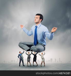 Meditating businessman. Young businessman sitting in lotus pose and supported by colleagues