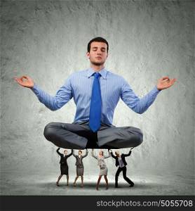 Meditating businessman. Young businessman sitting in lotus pose and supported by colleagues