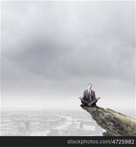 Meditating businessman. Young businessman sitting lotus pose on edge of rock mountain