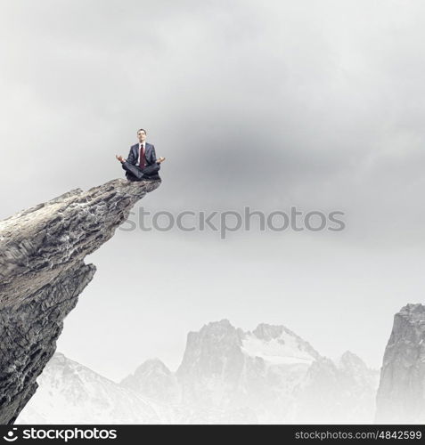 Meditating businessman. Young businessman sitting lotus pose on edge of rock mountain