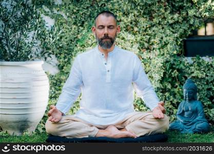 Meditating man. Peaceful man sitting in a lotus position and meditating in the garden.. Peaceful Man Meditating, Sitting in Lotus Position.