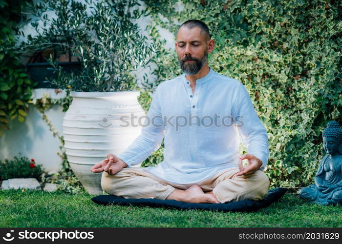 Meditating man. Peaceful man sitting in a lotus position and meditating in the garden.. Peaceful Man Meditating, Sitting in Lotus Position.