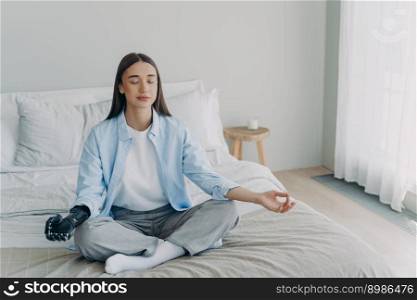 Meditation and concentration. Morning routine of disabled woman. Girl is sitting in lotus pose in her bedroom. Attractive european woman has artificial cyber limb. Stress relief at home.. Meditation and concentration. Morning routine of disabled woman with artificial cyber limb.