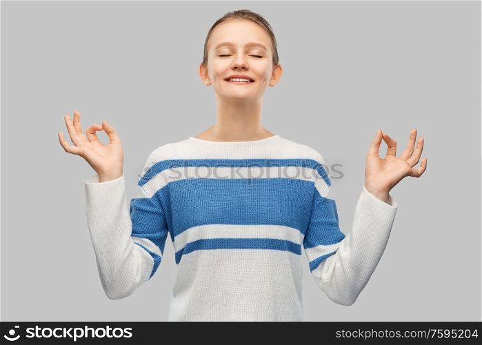 meditation and mindfulness people concept - happy smiling teenage girl in pullover meditating over grey background. happy smiling teenage girl in pullover meditating