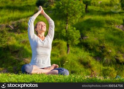 Meditation and relaxation yoga outdoors - young woman meditating and relaxing in Padmasana Lotus Pose) on green grass in forest. Young sporty fit woman doing yoga Lotus pose oudoors