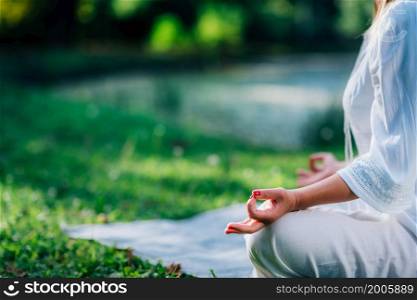 Meditation by the water, lotus position, green background. Woman Meditating by the Water, Sitting in Lotus Position.