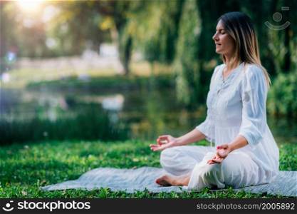 Meditation by the water, lotus position, green background. Woman Meditating by the Water, Sitting in Lotus Position.