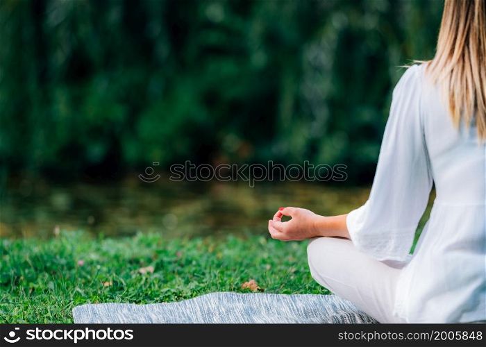 Meditation by the Water. Young woman meditating by the water, relaxation after yoga practice, green nature background.. Meditation by the Water.
