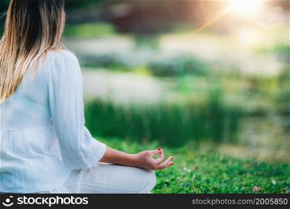 Meditation by the Water. Young woman meditating by the water, relaxation after yoga practice, green nature background.. Meditation by the Water.