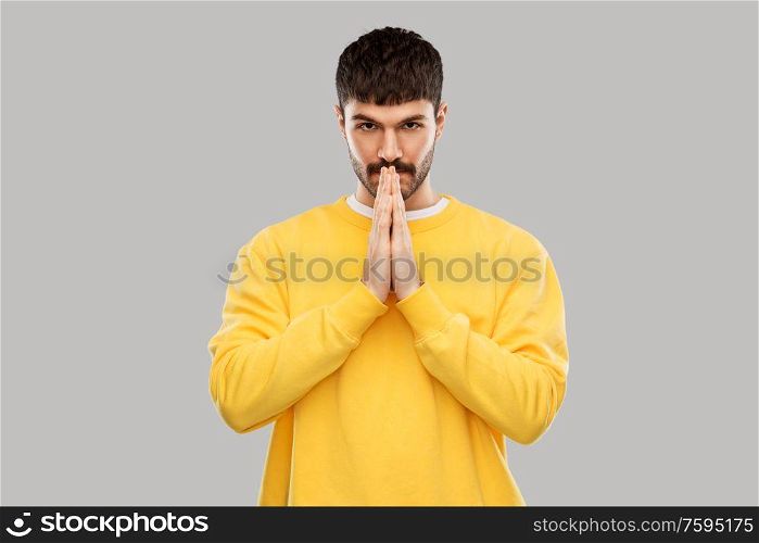 meditation, faith and mindfulness concept - young man in yellow sweatshirt praying or giving thanks over grey background. man in yellow sweatshirt praying or giving thanks
