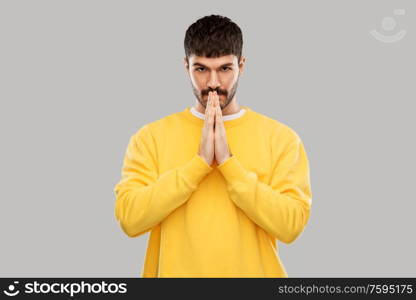 meditation, faith and mindfulness concept - young man in yellow sweatshirt praying or giving thanks over grey background. man in yellow sweatshirt praying or giving thanks