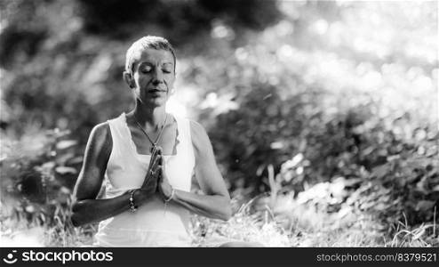Meditation in Nature - Mindful woman meditating, sitting on the ground with hands in a prayer position, eyes closed, embracing the positive aspects of nature, bathing in sunlight. Meditation in Nature