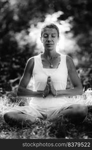 Meditation in Nature – Mindful woman meditating, sitting on the ground with hands in a prayer position, eyes closed, embracing the positive aspects of nature, bathing in sunlight. Meditation in Nature