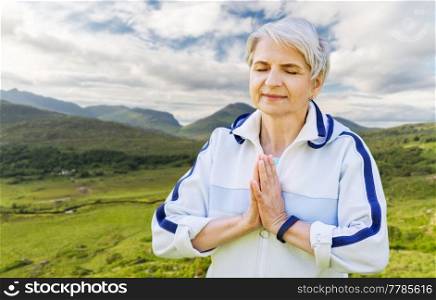meditation, mindfulness and healthy lifestyle concept - happy smiling senior woman doing yoga over Killarney National Park valley in ireland background. happy senior woman doing yoga at summer park