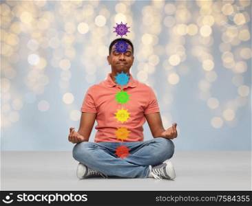 meditation, mindfulness and people concept - happy indian man meditating in lotus yoga pose with seven chakra symbols over festive lights background. happy indian man meditating in lotus yoga pose