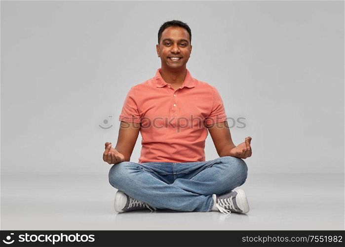 meditation, mindfulness and people concept - happy indian mant meditating in lotus yoga pose over gray background. happy indian mant meditating in lotus yoga pose