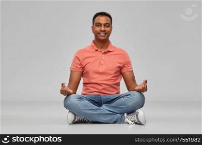 meditation, mindfulness and people concept - happy indian mant meditating in lotus yoga pose over gray background. happy indian mant meditating in lotus yoga pose