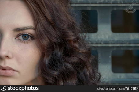 Meditative girl half face in front of metal grid looking at camera, copyspace. Broody girl half face in front of metal grid looking at camera