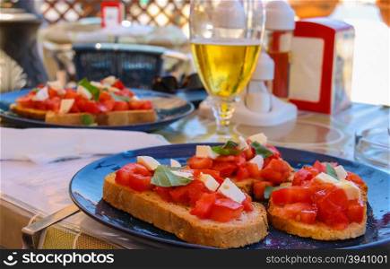 Mediterranean cuisine restaurant - sandwiches with tomatoes and cheese on plate and glass of light beer