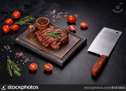Medium rare sliced grilled striploin beef steak served on wooden board. Grilled ribeye beef steak, herbs and spices on a dark table
