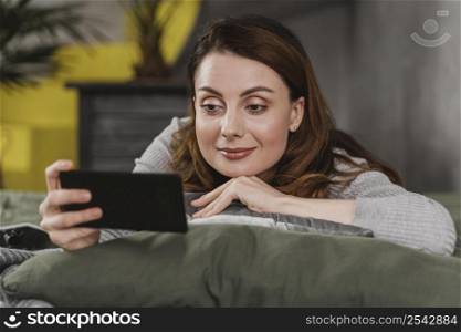 medium shot woman bed with phone