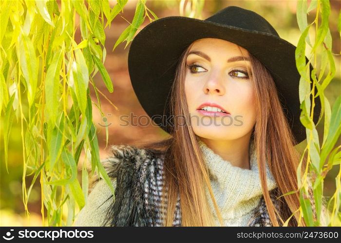 Meeting time. Trendy young woman waiting for someone in park around green leaves of willow tree.