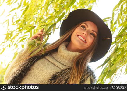 Meeting time. Trendy young woman waiting for someone in park around green leaves of willow tree.