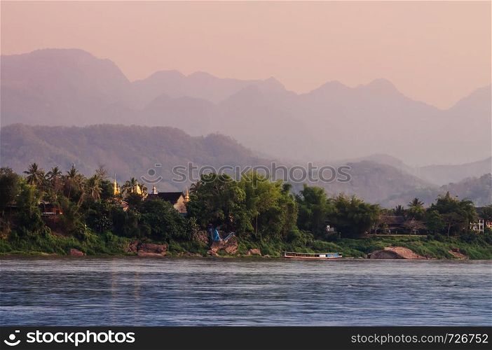 Mekhong or Mae Khong river view and Old aged Buddhist temple with lush green forest and mountains in Luang Prabang, Laos under evening sky