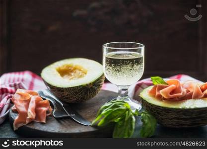 Melon half and ham with wine on rustic table at dark background, front view, place for text, border