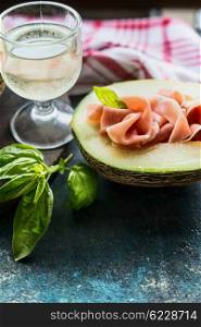Melon with ham and glass of white wine on rustic background. Italian food concept