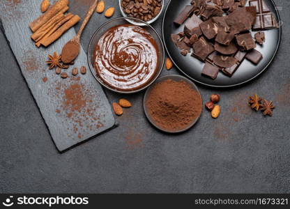 Melted chocolate or Hazelnut spread in glass bowl and chocolate pieces on dark concrete background or table. Melted chocolate or Hazelnut spread in glass bowl and chocolate pieces on dark concrete background