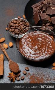 Melted chocolate or Hazelnut spread in glass bowl and chocolate pieces on dark concrete background or table. Melted chocolate or Hazelnut spread in glass bowl and chocolate pieces on dark concrete background