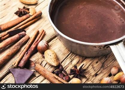 Melting chocolate in a metal bowl. bowl with melted hot chocolate, cocoa beans, nuts and spices
