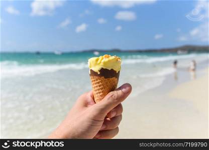 Melting ice cream on beach in summer hot weather ocean landscape nature outdoor vacation , Yellow ice cream mango with nuts / Ice cream cone in hand with sea background