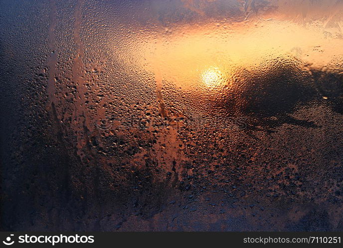 Melting ice, water drops and sunlight on a window pane on a winter morning, close-up natural texture