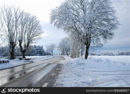 Melting snow and ice on a country road through a wintry landscape