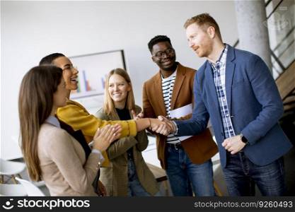 Memembers of young creative team shaking hands while working in the modern office