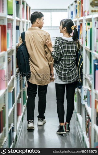 Men and women carrying a backpack and searching for books in the library.