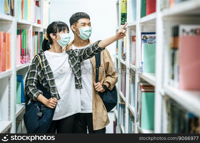 Men and women carrying a backpack and searching for books in the library.