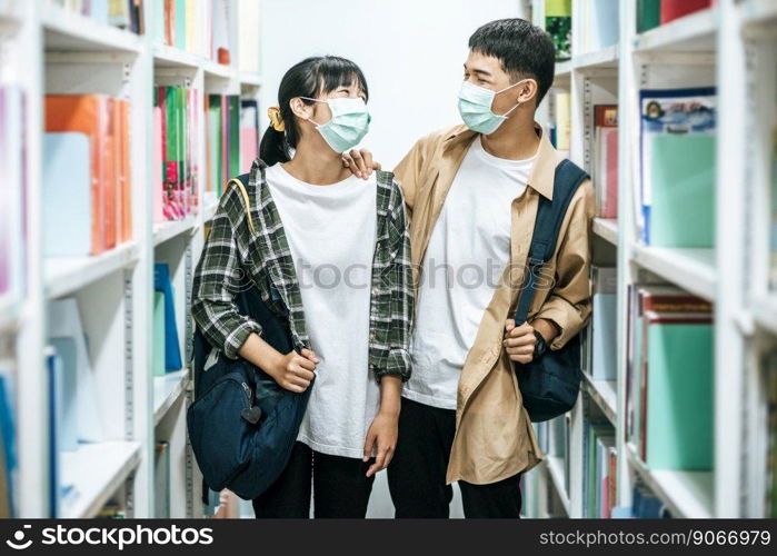 Men and women carrying a backpack and searching for books in the library.